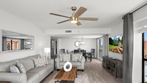 Un salon spacieux avec un canapé gris, une table basse en bois et un ventilateur de plafond.