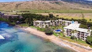 Un hotel sulla costa con diversi edifici, una spiaggia e turbine eoliche sullo sfondo.