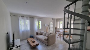 Un ampio soggiorno con divano, tavolino e televisore su un mobile. Una scala conduce a un livello superiore.