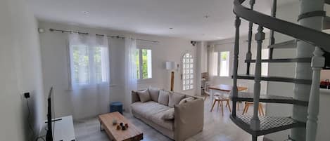 A spacious living room with a sofa, coffee table, and a TV on a stand. A staircase leads to an upper level.