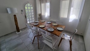 Zona pranzo con tavolo in legno, sedie bianche e una porta a vetro con motivo a griglia.