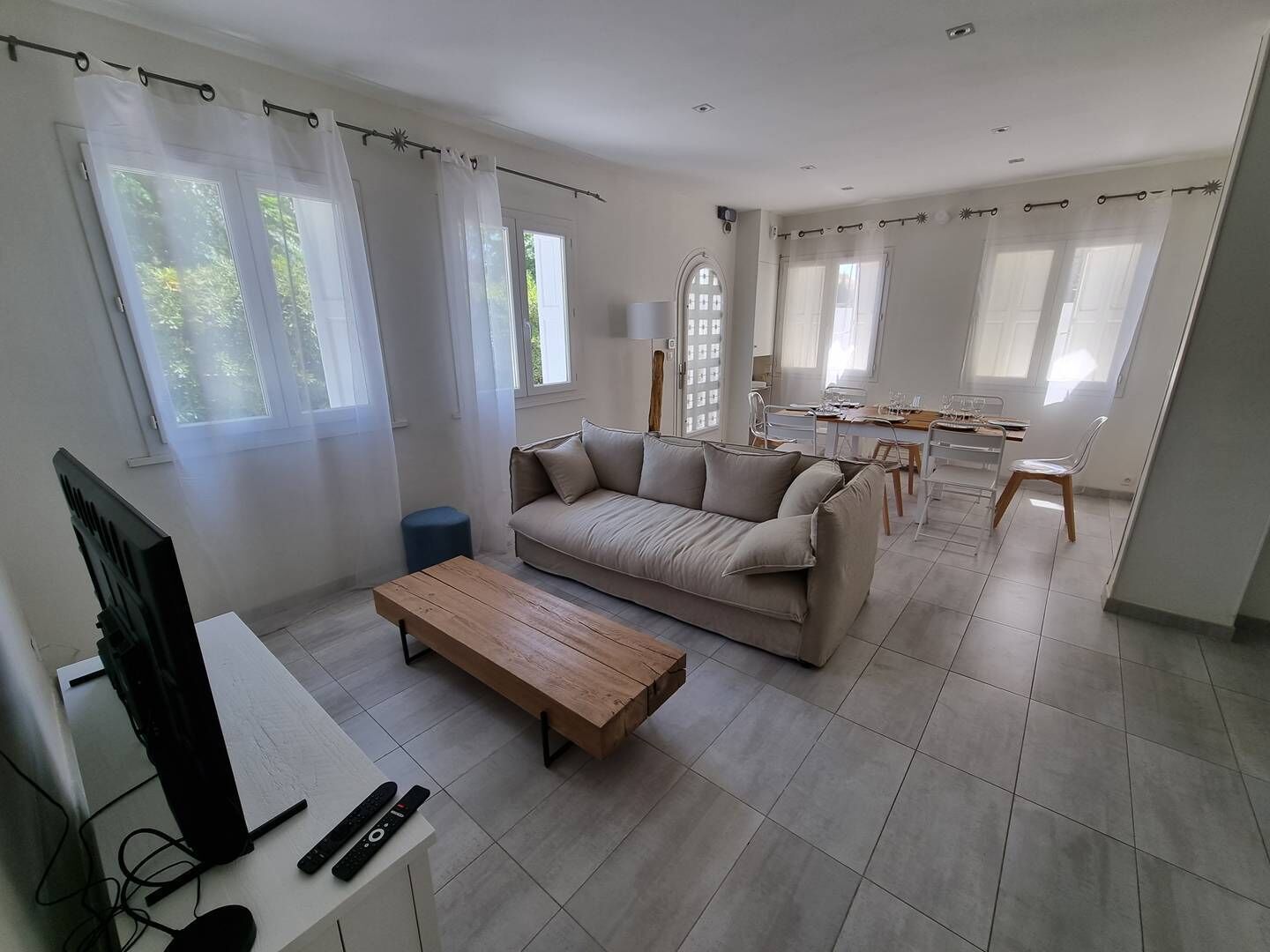 A modern living room with a sofa, coffee table, and TV. There is a dining area with a table and chairs.