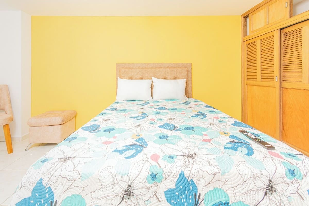 A bedroom with a bed, two pillows, a wooden wardrobe, and a small chair.