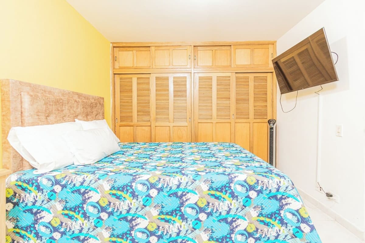 A bedroom with a bed, wooden wardrobe, and a television mounted on the wall.