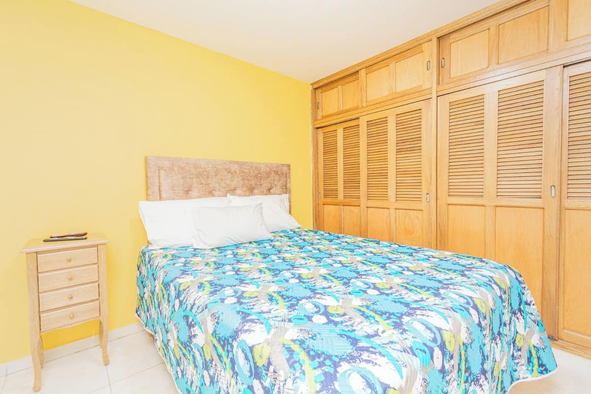 A bedroom with a bed, a nightstand, and a wooden wardrobe.