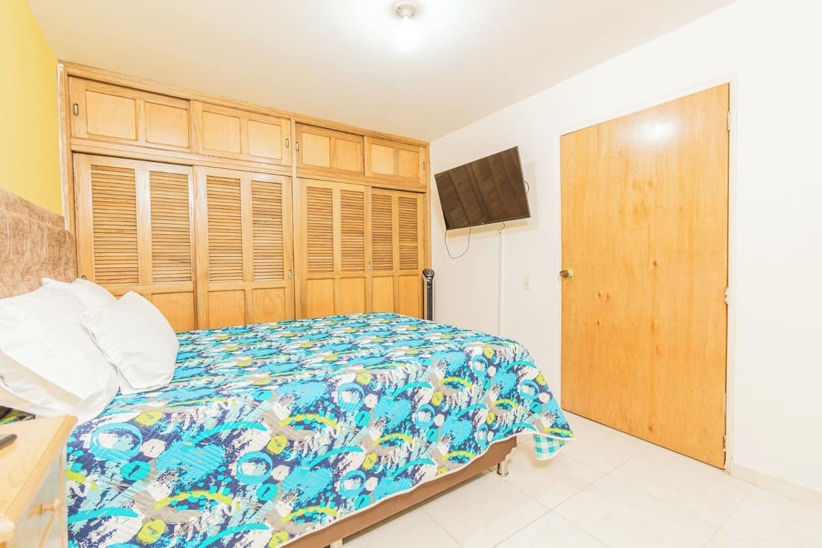 A bedroom with a bed, wooden wardrobe, and a television on the wall.