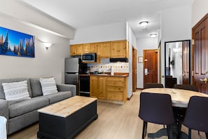 A modern kitchen with wooden cabinets, a microwave, and a refrigerator. There is a dining table with chairs and a gray sofa with decorative pillows. - Hearthstone Lodge #219 (Sun Peaks)