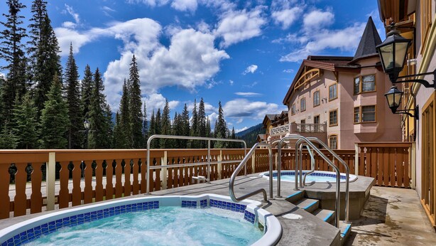 A hot tub with a wooden deck, a metal staircase, and a view of a mountain and forest.
