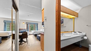 A hotel room with a large bed, a desk, and a bathroom with a sink and mirror.