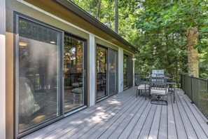 A wooden deck with outdoor furniture, large sliding glass doors, and a grill area.