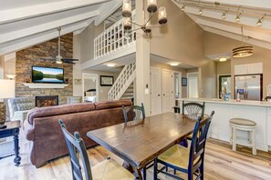 A spacious living area with a fireplace, a large wooden dining table, and a high ceiling with exposed beams.