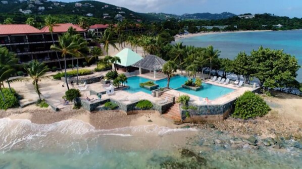 A resort with a swimming pool, beach, and palm trees.
