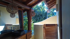 Une salle de bain avec un meuble-lavabo en bois, un évier noir et une fenêtre donnant sur un jardin tropical.