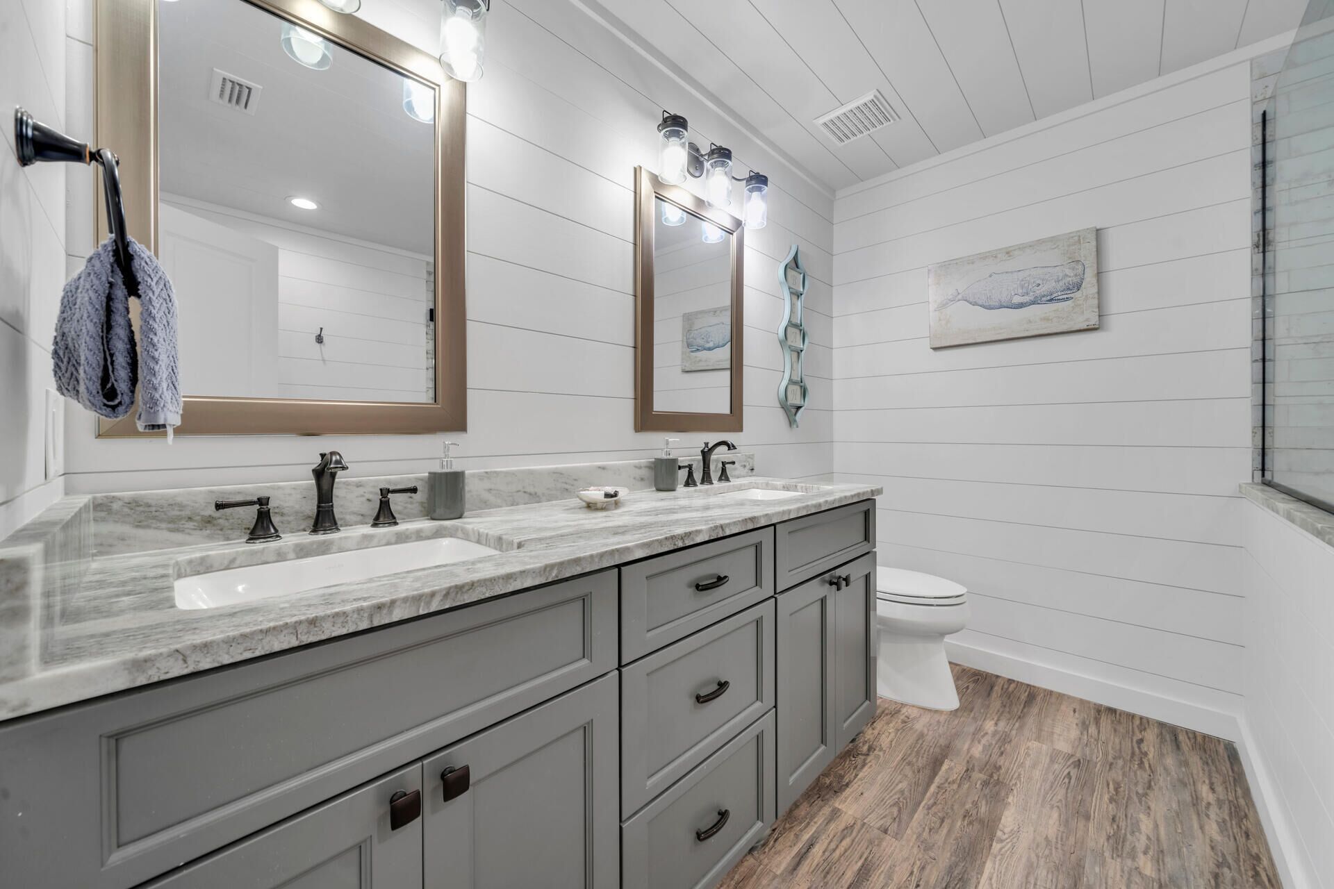 A bathroom with a double sink vanity, a toilet, and a large mirror with lights.