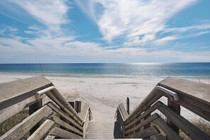 A wooden boardwalk leading to a beach with a clear view of the ocean.