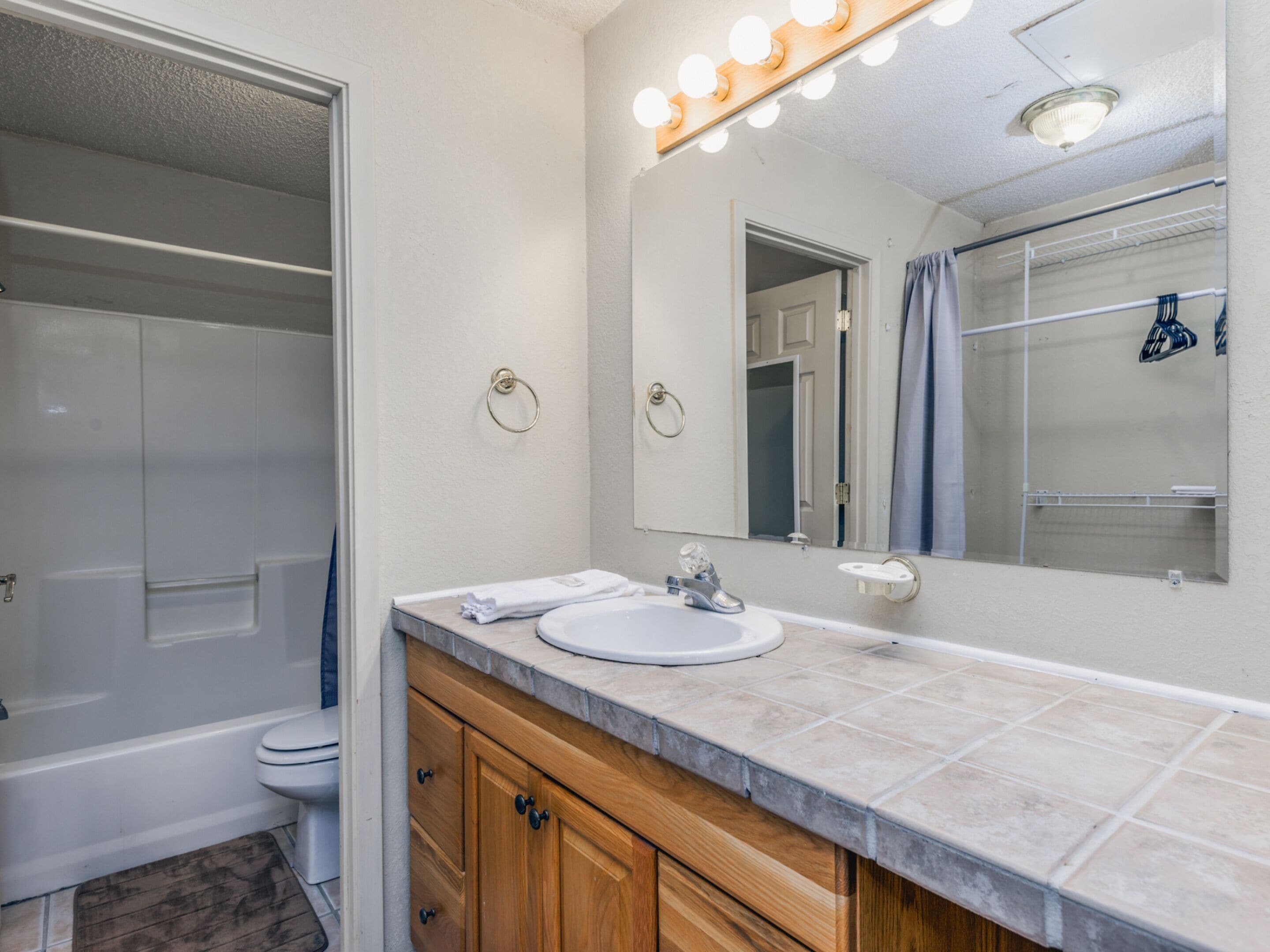 A bathroom with a vanity, sink, and mirror. There is a shower curtain and a towel rack.
