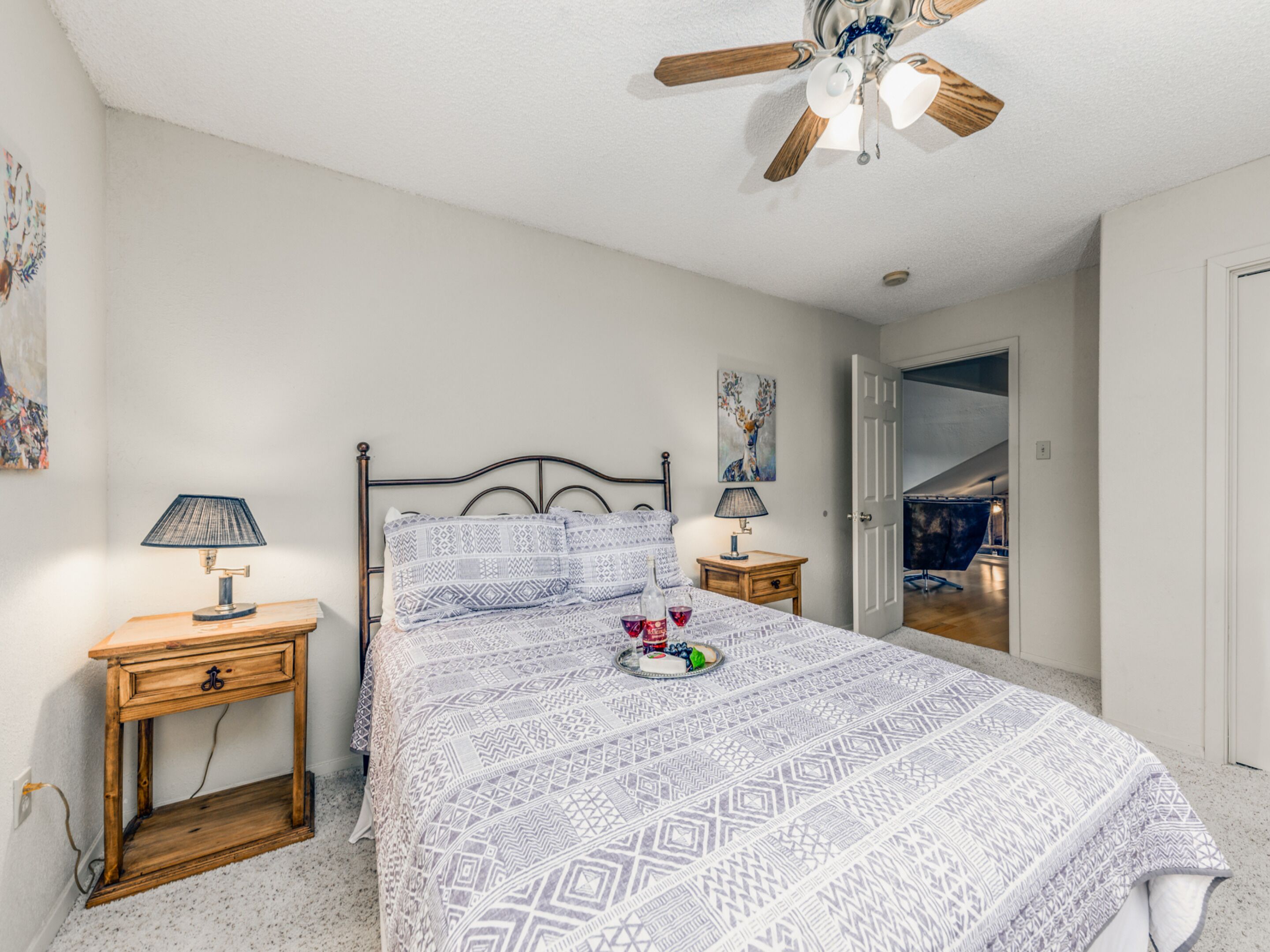 A bedroom with a bed, two bedside tables, a ceiling fan, and a door leading to another room.