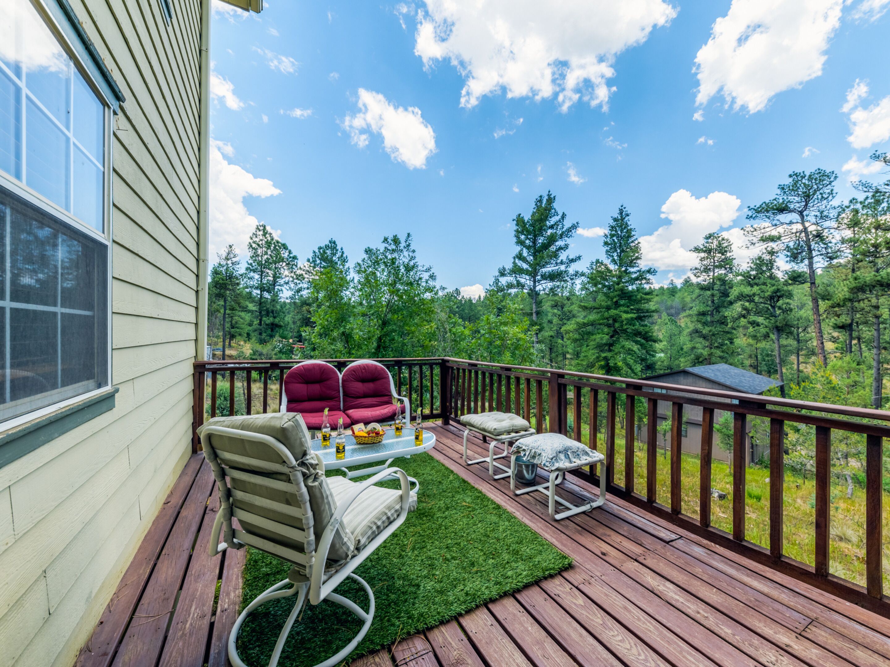 A deck with outdoor furniture, a small table with drinks, and a view of a forest.