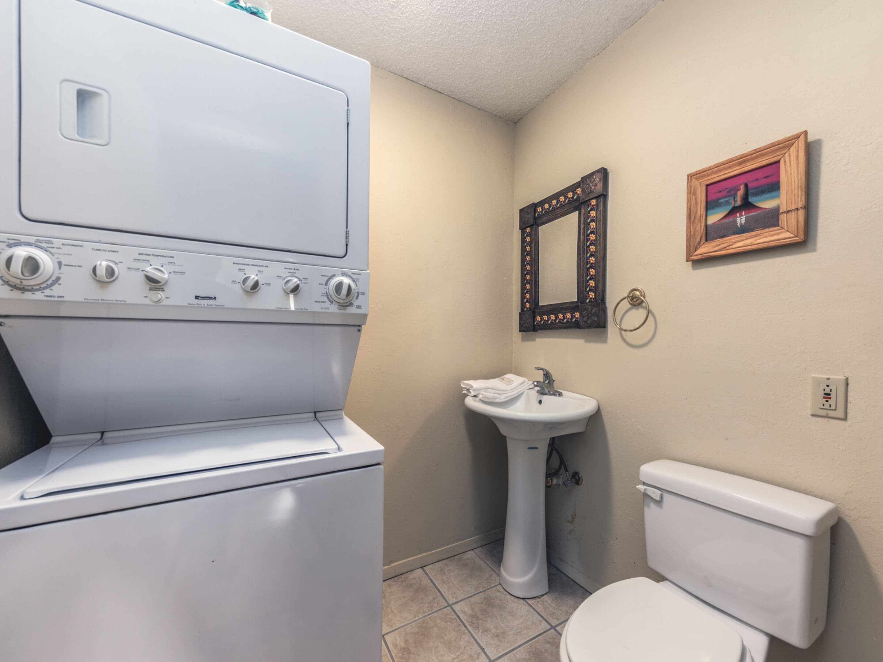A compact bathroom with a white washing machine, a pedestal sink, and a toilet.