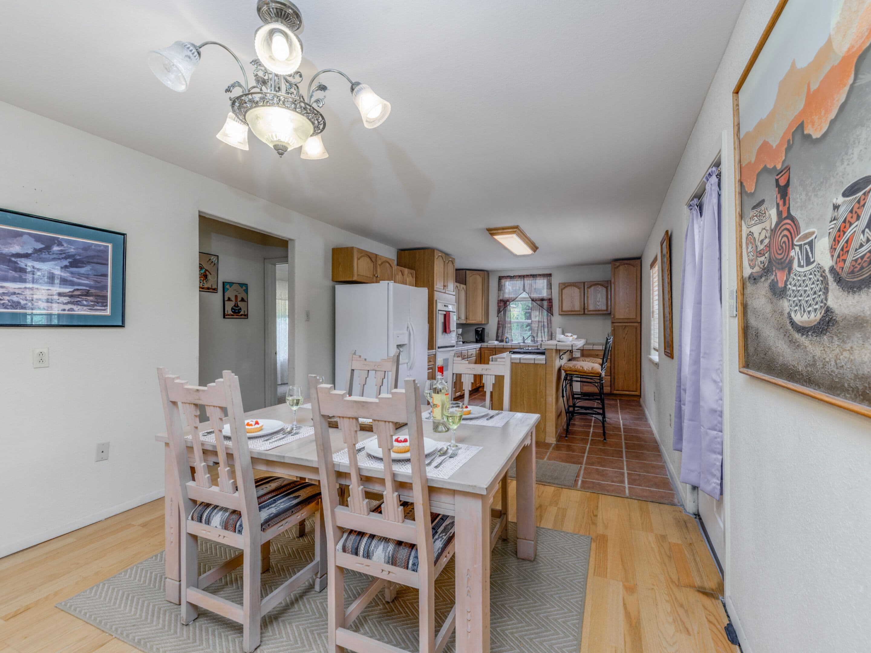 A modern kitchen with wooden cabinets, a white refrigerator, and a dining area with a wooden table and chairs.