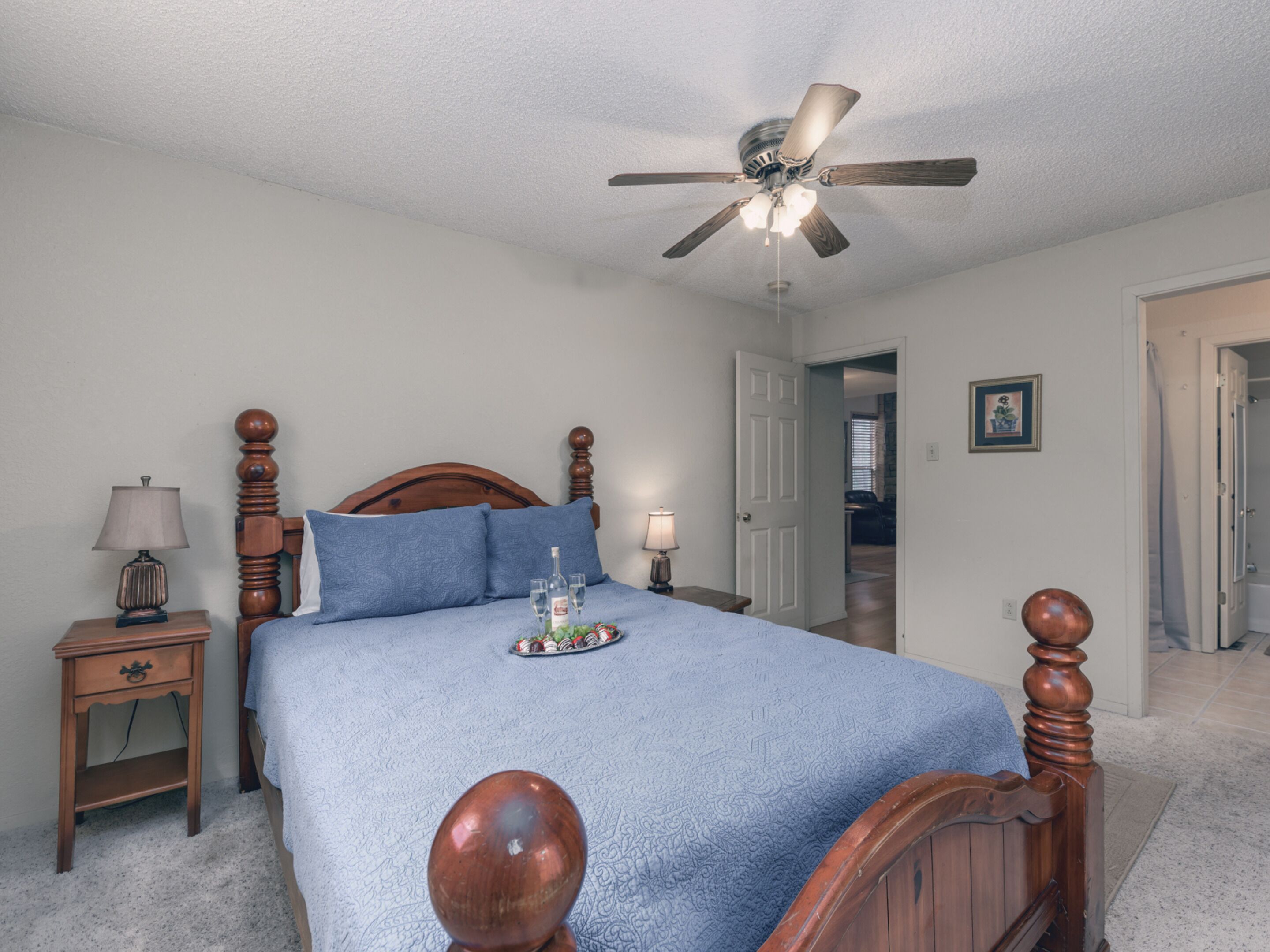 A bedroom with a wooden bed, a ceiling fan, a nightstand, and a bedside table with a lamp.