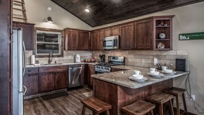 Una cucina moderna con mobili in legno scuro, elettrodomestici in acciaio inossidabile, un piano di lavoro in granito e un'area bar con sgabelli.