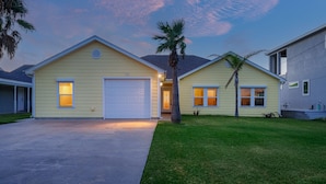 A two-story residential house with a garage, a lawn, and palm trees.