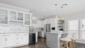 A modern kitchen with white cabinetry, a central island, and a bar area with stools.