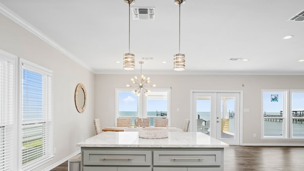 A spacious kitchen with a large island, pendant lighting, and a view of the ocean through large windows.