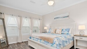 A bedroom with a large bed, two bedside tables with lamps, a ceiling fan, and a window with curtains. - The Castaway by Miss Kitty’s (Rockport)