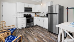 A modern kitchen with white cabinets, stainless steel appliances, a wooden floor, and a ceiling fan. - The Castaway by Miss Kitty’s (Rockport)