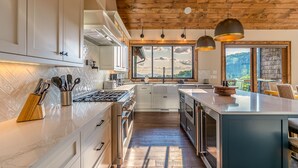 A modern kitchen with a large island, wooden ceiling, and a view of the outdoors. - Up & Away at Eagles Nest | Luxury Mountain Home | Sleeps 24 | Views + Hot Tub (Banner Elk)