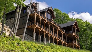 A multi-story log cabin with a stone foundation, wooden balconies, and large windows. - Up & Away at Eagles Nest | Luxury Mountain Home | Sleeps 24 | Views + Hot Tub (Banner Elk)