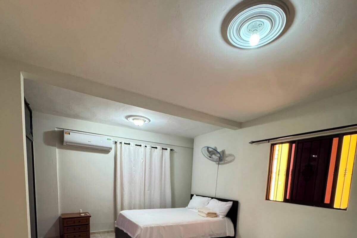A hotel room with two beds, a ceiling fan, an air conditioning unit, and a patterned floor.