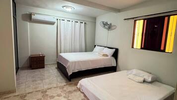 A hotel room with two beds, a ceiling fan, an air conditioning unit, and a patterned floor.