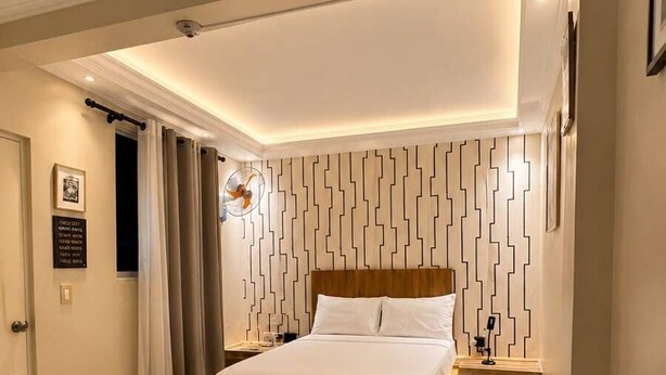 A modern bedroom with a bed, bedside tables, a potted plant, and a wall with a geometric pattern. - Hotel 1325 (Bani)