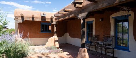A traditional adobe building with a covered patio area, stone pathway, and outdoor seating.