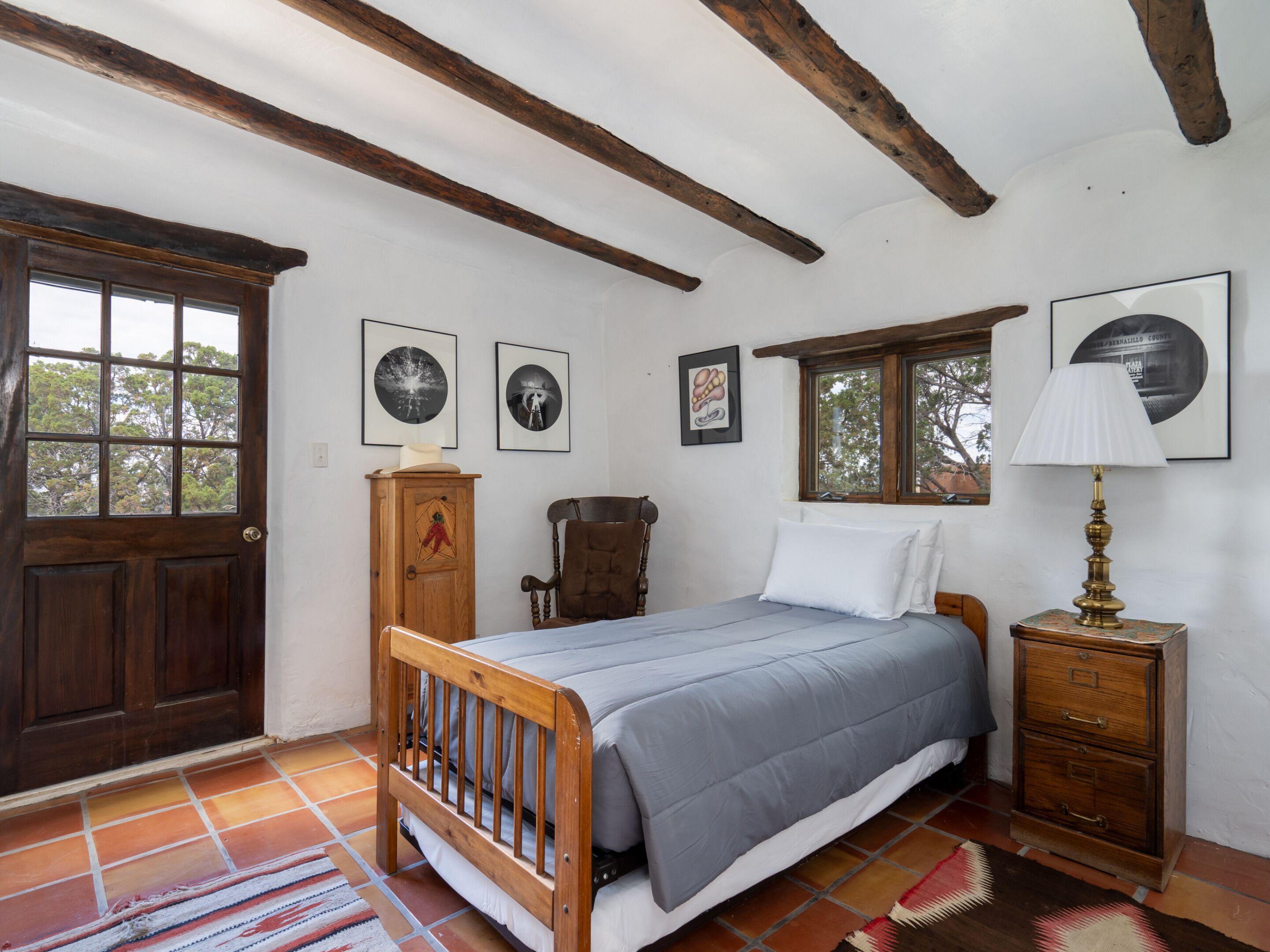 A bedroom with a wooden bed, a nightstand, a lamp, and a window with a view of trees.
