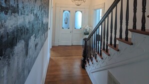A hallway with a wooden floor, white walls, a chandelier, and a staircase with dark balusters.