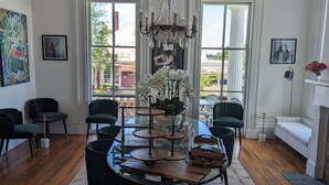 A dining area with a round glass table, black chairs, a chandelier, and a view of the outside through large windows.