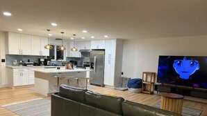 A modern living room with a leather sofa, a TV, and a kitchen in the background. - Private Lake House (Puyallup)
