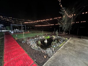 A garden area with a pond, red patterned walkway, and string lights.