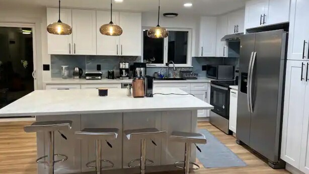 A modern kitchen with a central island, bar stools, stainless steel appliances, and pendant lighting. - Private Lake House (Puyallup)