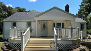Ein eingeschossiges Haus mit Veranda, Schornstein und einer kleinen Terrasse mit Geländer.
