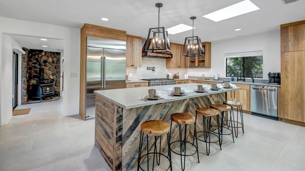 A modern kitchen with a large island, bar stools, a stone fireplace, and a large window.