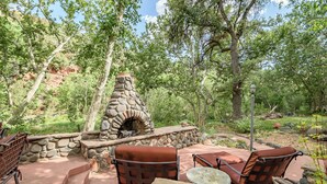 An outdoor patio with stone seating, a stone fireplace, and surrounding greenery.