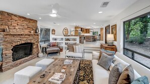 A spacious living room with a stone fireplace, a large dining area, and a kitchen in the background.