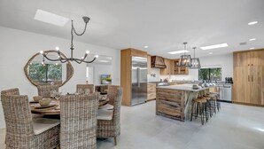 A modern kitchen with a central island, stainless steel appliances, and a dining area with wicker furniture.