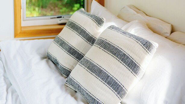A bedroom with a large window, a bed with white bedding, and a striped pillow. - The Cabins at Reverence Farms by Sagra (Graham)