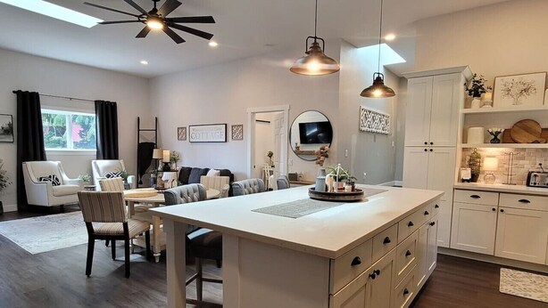 A modern kitchen with white cabinetry, a central island, pendant lighting, and a dining area with a sofa and chairs. - Coal Creek Cottage (hot tub, dog and kid friendly) (Sedro-Woolley)